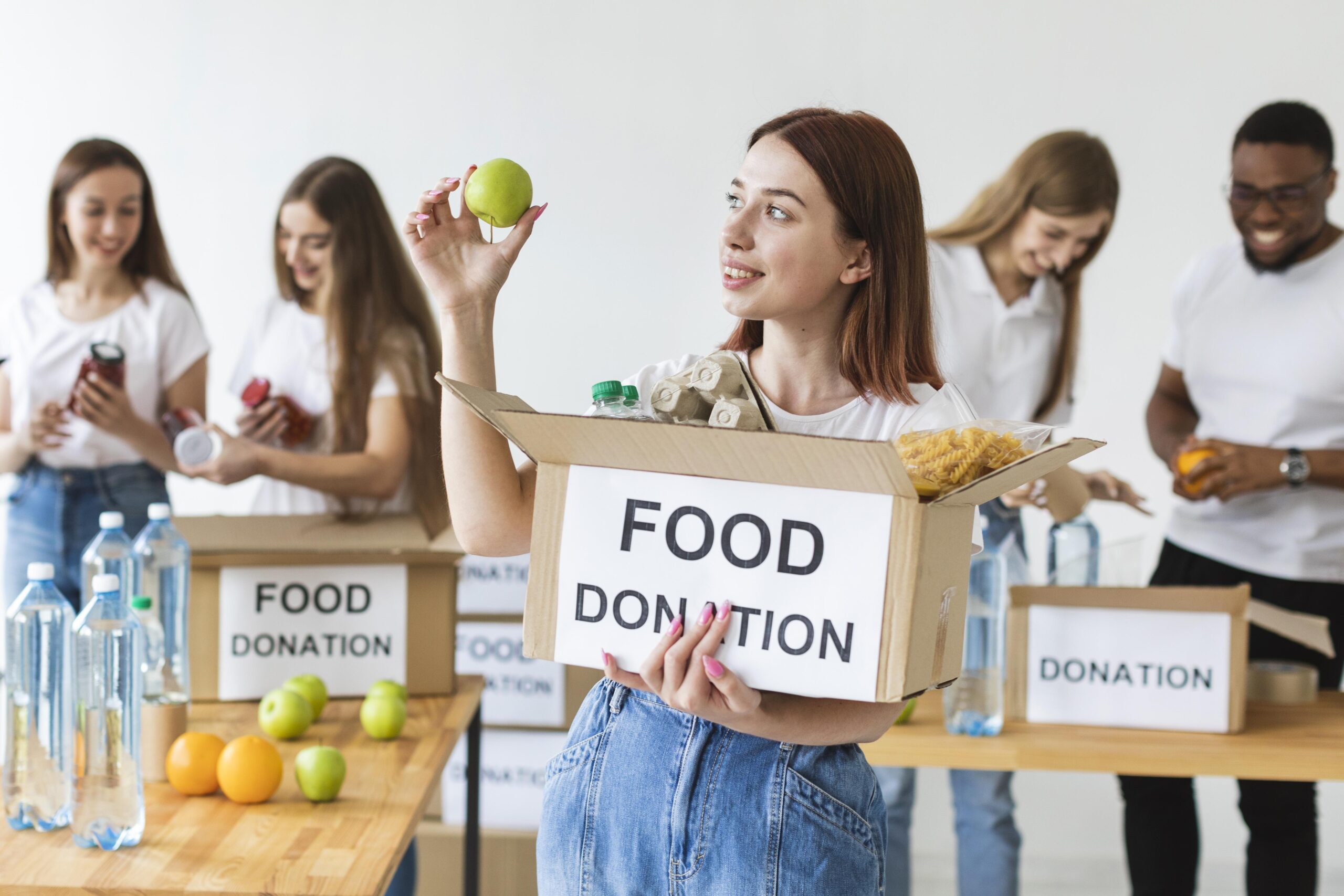 smiley-female-volunteer-holding-food-donations-box-with-apple