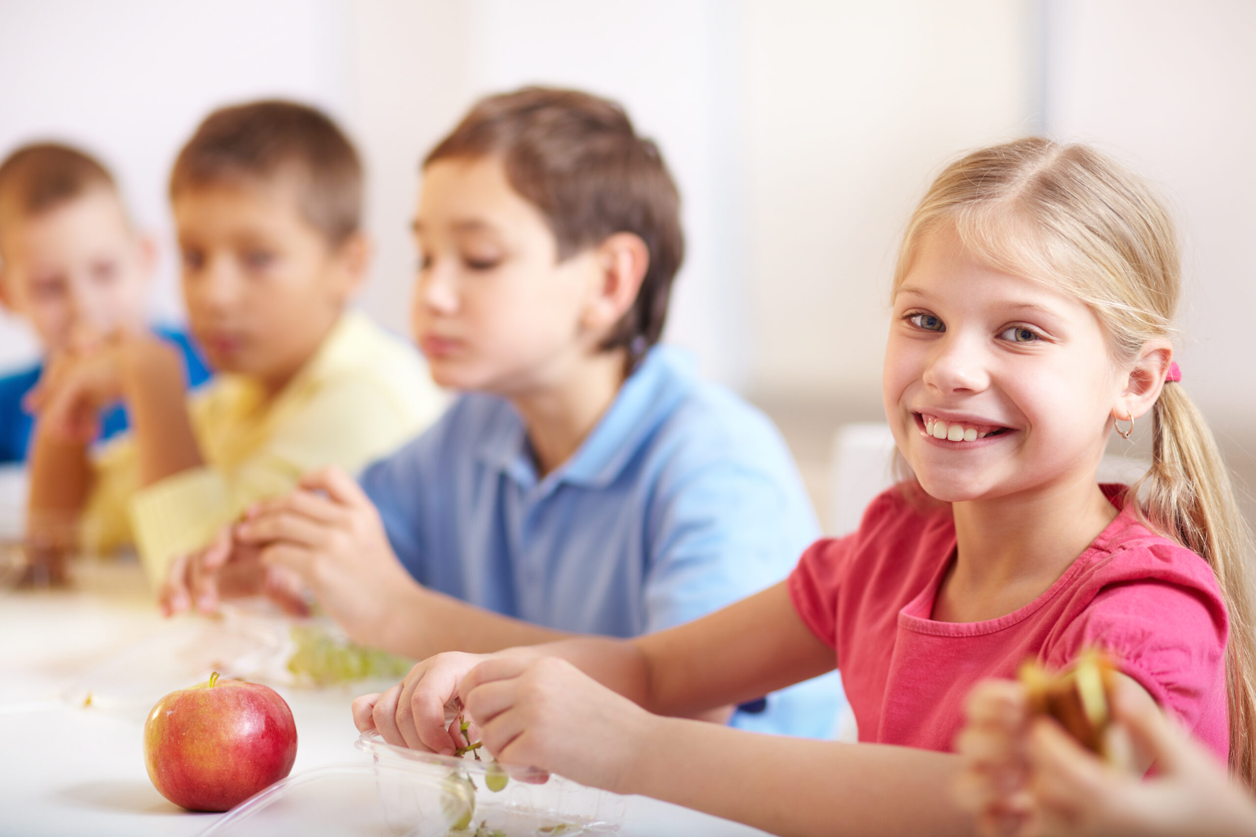 Group of kids having lunch during break with focus on smiling girl looking at camera